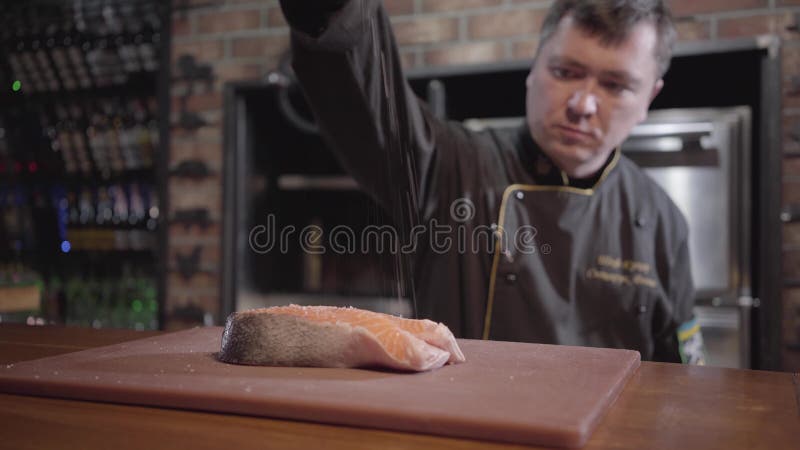 Шеф-повар портрета брызгая соль и перец на сырцовой части рыб marinated и готовых быть зажаренным в гриле позже